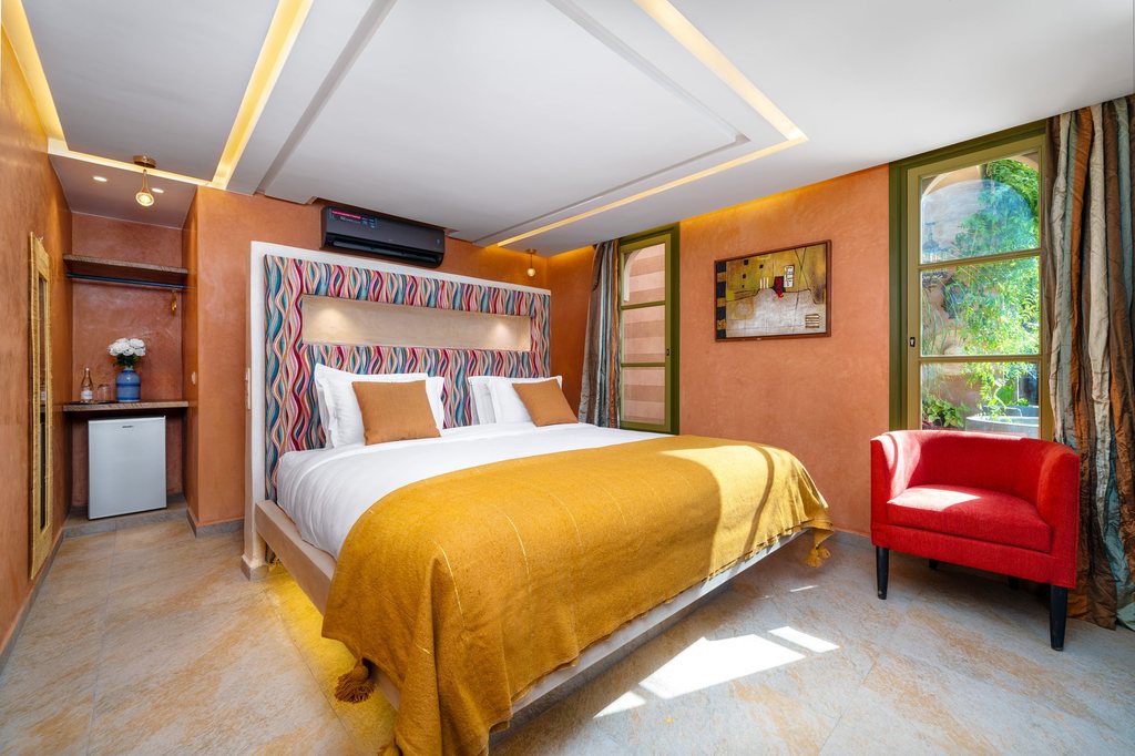 Bed dressed in white linen beneath a handcrafted Moroccan headboard, saffron throw